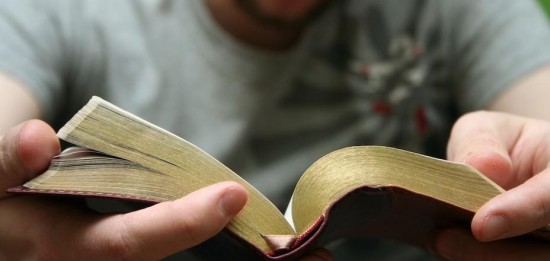 Young blond man reading the Bible with bright green background